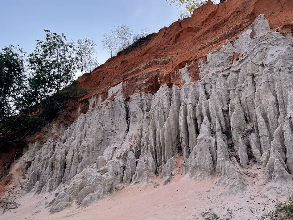 The red sandstone canyon section of Fairy Stream Mui Ne, showing layered orange-red sand formations rising on one side with green vegetation on the other