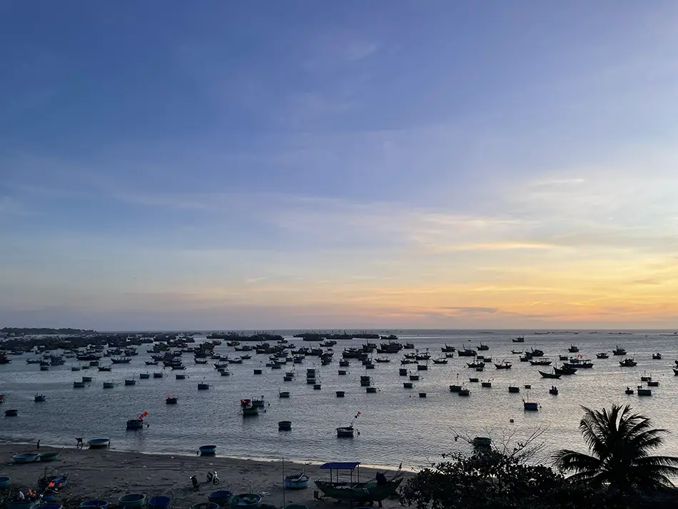 Silhouette of round basket boats scattered across calm water at the Mui Ne fishing village during sunset