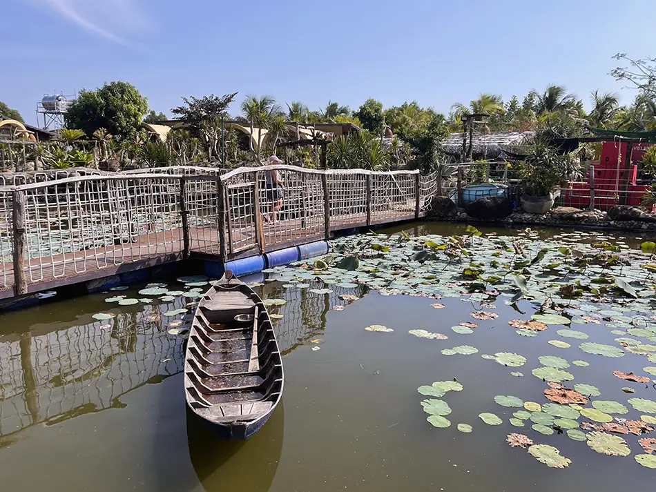 Wooden boat dock extending over a lotus-filled pond surrounded by lush tropical greenery at Gai Garden Café, a hidden garden retreat near Mui Ne
