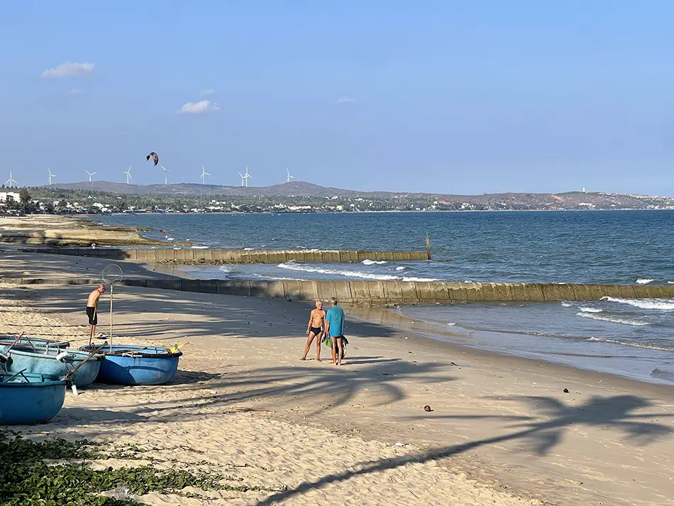 Tourists and fishing boats scattered across the main Mui Ne beach strip on a clear day, with hotels visible in the background