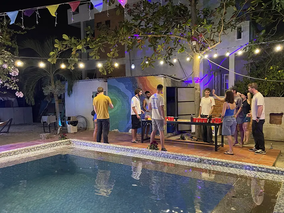 Travelers gathered around a lit pool area at iHome hostel in Mui Ne with string lights overhead and people socializing at the bar — a typical evening when backpacking Mui Ne