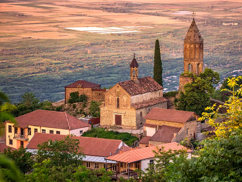 The medieval fortified walls and terracotta-roofed buildings of Sighnaghi, with green vineyards and hills in the late afternoon light