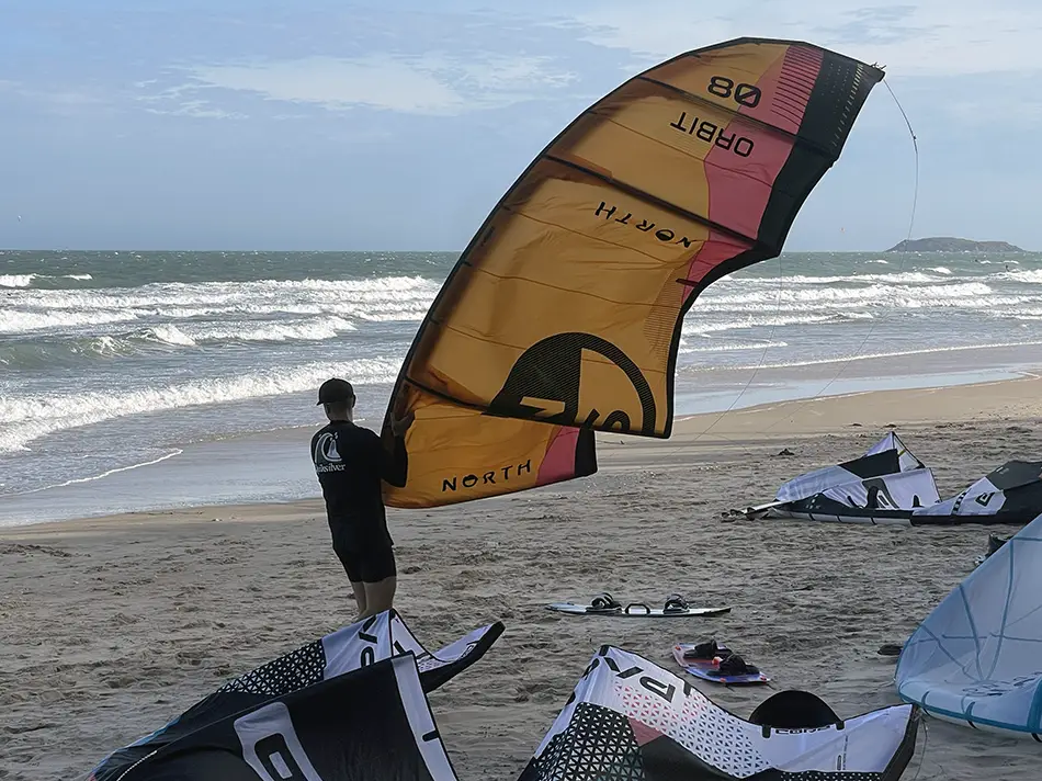 Kitesurfing equipment and colorful kites laid out on a windy beach in Mui Ne with riders preparing near the shoreline