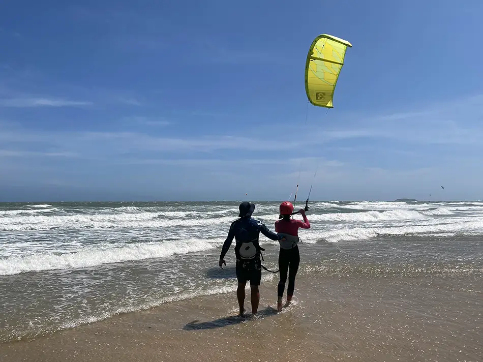 nstructor and student handling a yellow training kite on the sand during a kitesurfing lesson at Mui Ne beach