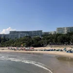 Sandy beach curving along the Ham Tien coastline with low-rise hotels and palm trees lining the shore