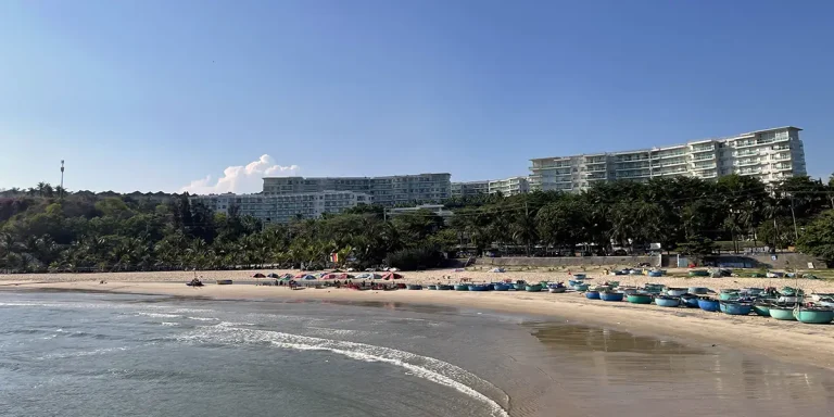 Sandy beach curving along the Ham Tien coastline with low-rise hotels and palm trees lining the shore