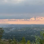 Sweeping panoramic view of Mui Ne's coastline and village rooftops seen from an elevated vantage point at dusk, with pink and purple clouds reflected on the calm sea — a Mui Ne hidden gem known to few visitors