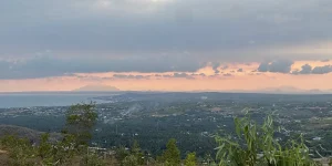 Sweeping panoramic view of Mui Ne's coastline and village rooftops seen from an elevated vantage point at dusk, with pink and purple clouds reflected on the calm sea — a Mui Ne hidden gem known to few visitors