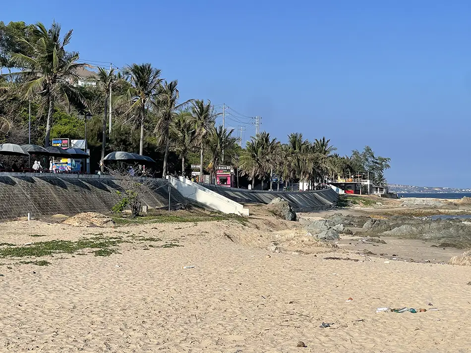 Wide sand flat exposed at low tide at Ong Dia Beach near Mui Ne, with coastal trees