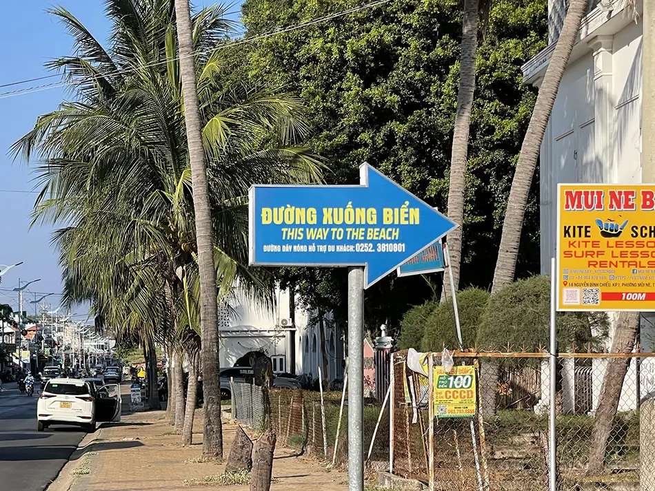Road sign pointing toward a public beach access path between hotels along the coast