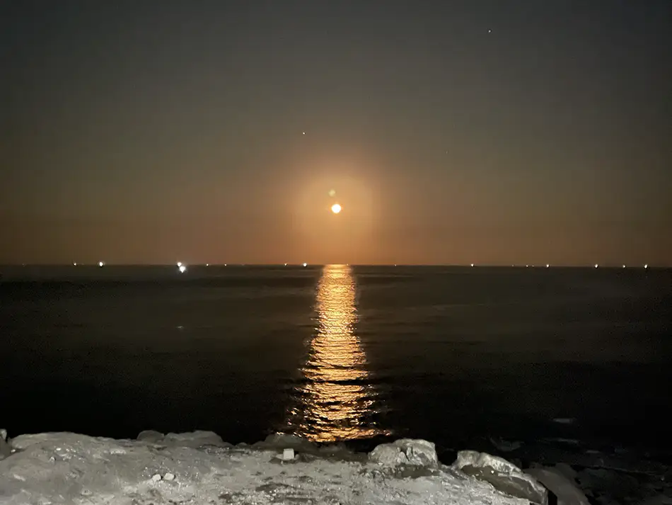 Full moon rising over open water as seen from the rocky headland near Miếu Bà Vàng shrine on the Mui Ne cape
