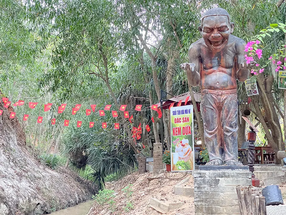 A quirky stream-side cafe at Fairy Stream decorated with painted wooden figures and red string lights, typical of commercial stalls along the walk