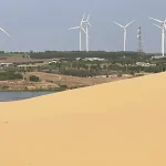 Row of wind turbines on green hills seen from the White Sand Dunes Mui Ne