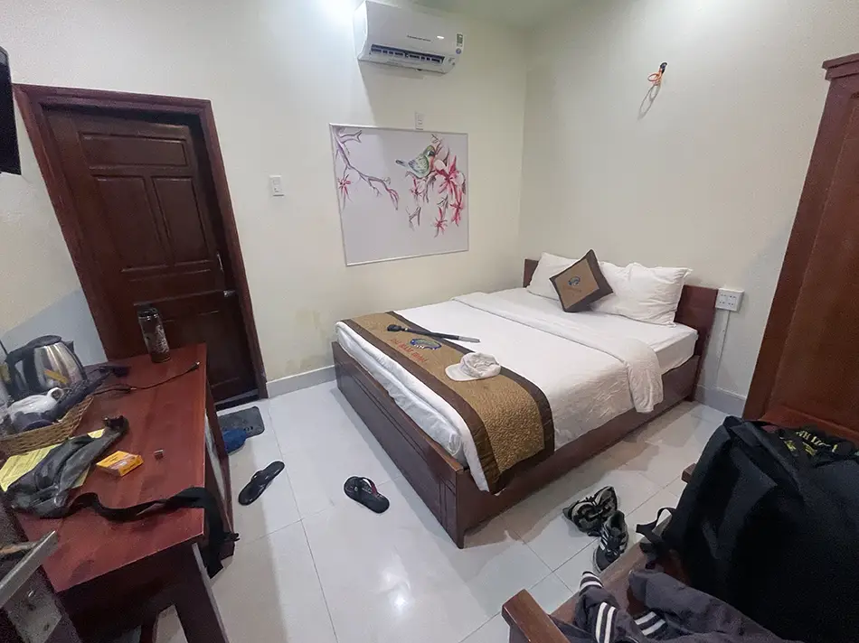 Interior of a budget Vietnamese hotel room featuring a large bed and a desk, but no windows.