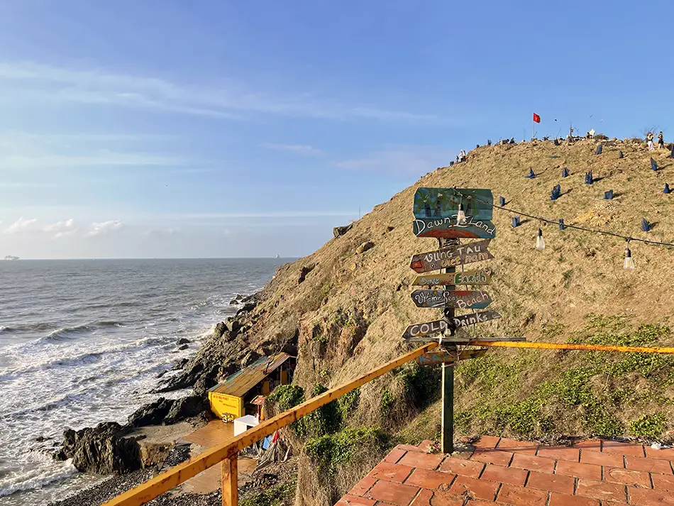 Rocky cliffs at Cape Nghinh Phong in Vung Tau with a yellow safety railing along the edge and visitors on the grassy ridge above the sea.