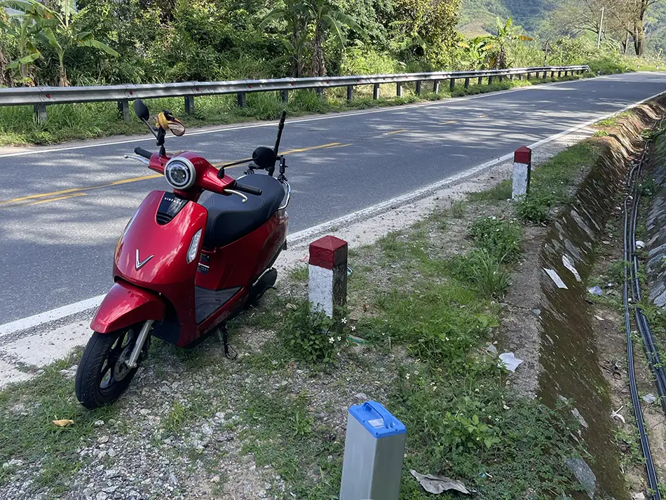 An electric scooter parked on the shoulder of a winding mountain road in Vietnam.