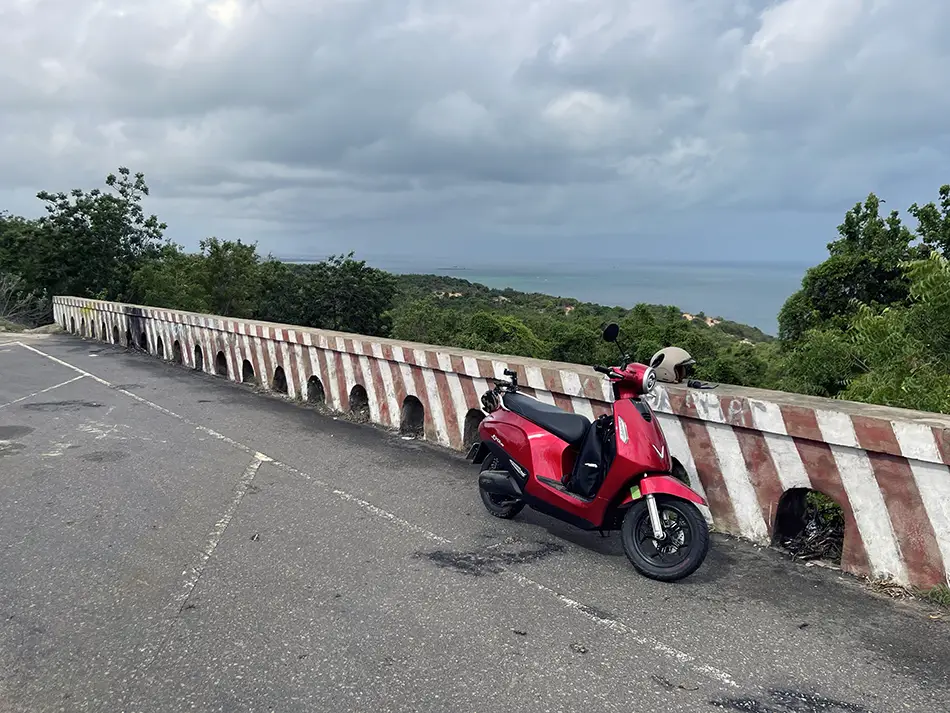 An electric scooter parked by a scenic road in Vietnam with a view of the sea.