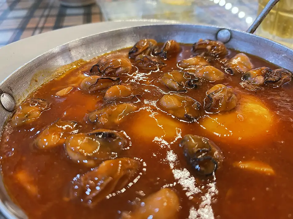 A metal bowl of hàu né, oysters cooked in a dark sizzling sauce, the signature seafood dish at Hàu né Tâm Nguyễn near Front Beach in Vung Tau.