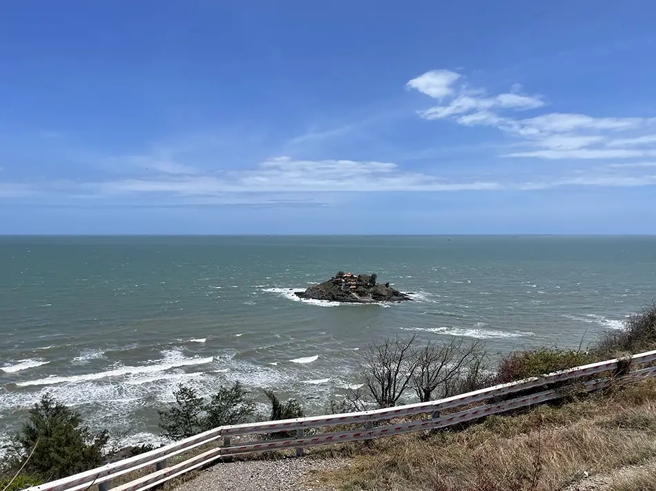 Small Hon Ba Shrine on a rocky outcrop offshore in Vung Tau, photographed from the coastal road railing at high tide.