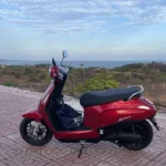 A red Electric scooter parked on a tiled coastal viewpoint in Vietnam, with the sea and a hazy horizon in the background.