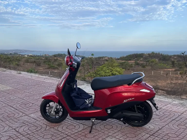 A red Electric scooter parked on a tiled coastal viewpoint in Vietnam, with the sea and a hazy horizon in the background.