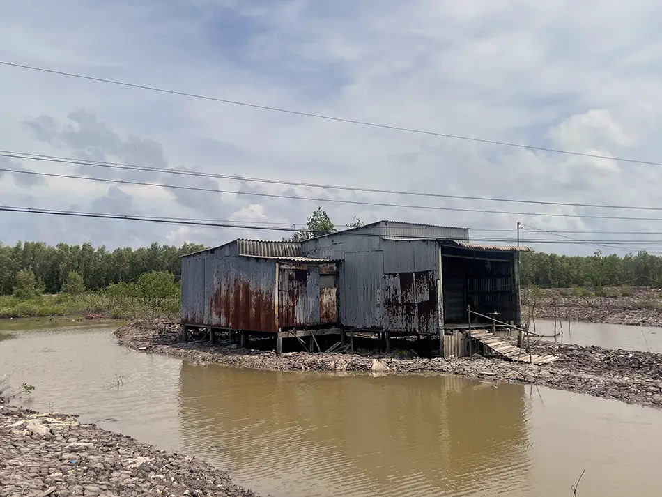 Small roadside house surrounded by muddy floodwater during a rural detour near Ca Mau, Vietnam.