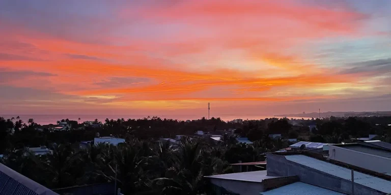 Orange and pink sunset over Mui Ne rooftops seen from a hillside viewpoint above town