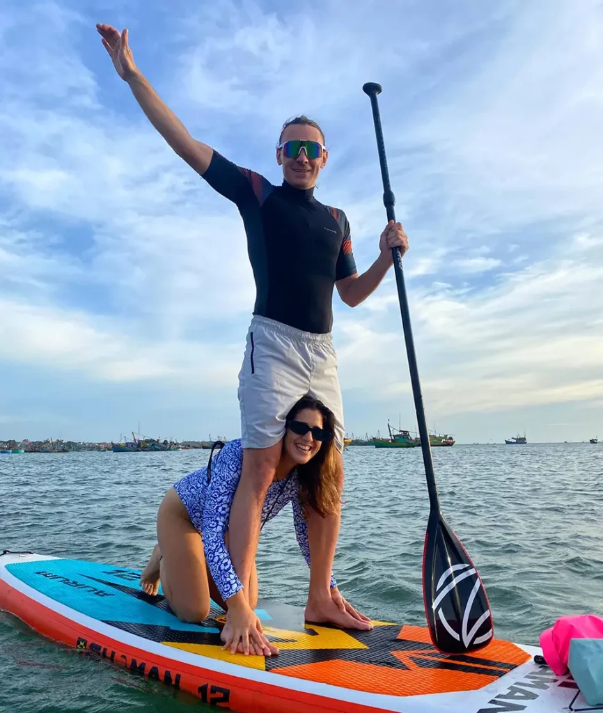 Couple paddling a stand-up paddleboard together on calm water near Mui Ne fishing village