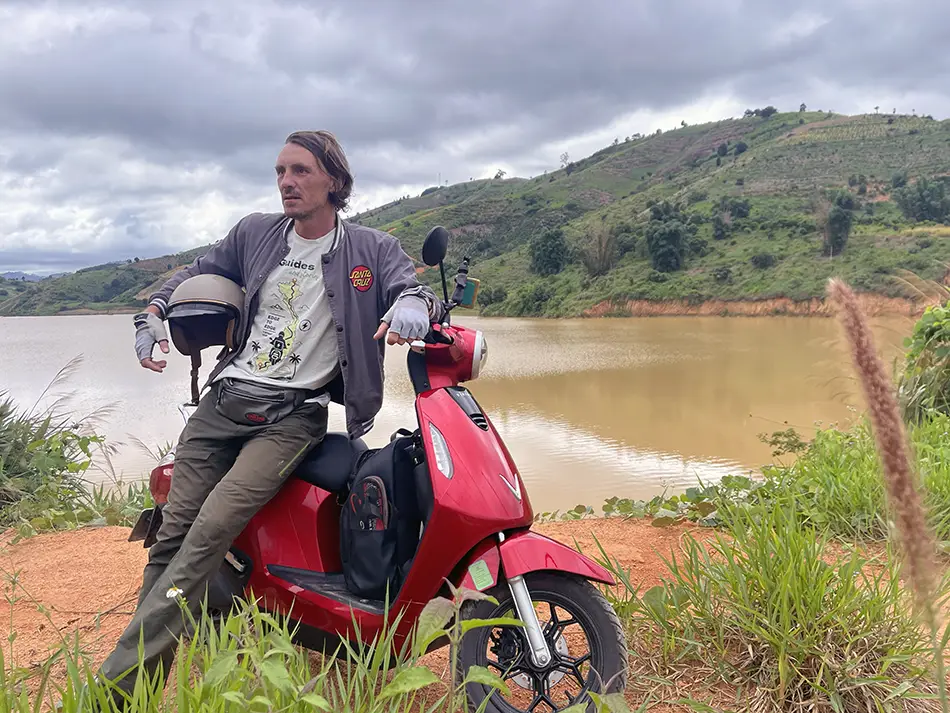 Yuri Malykh with his electric scooter overlooking a reservoir.