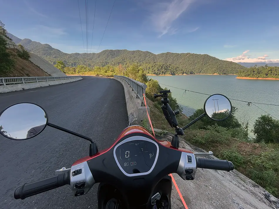 First-person view riding an electric scooter along a winding road overlooking a reservoir.