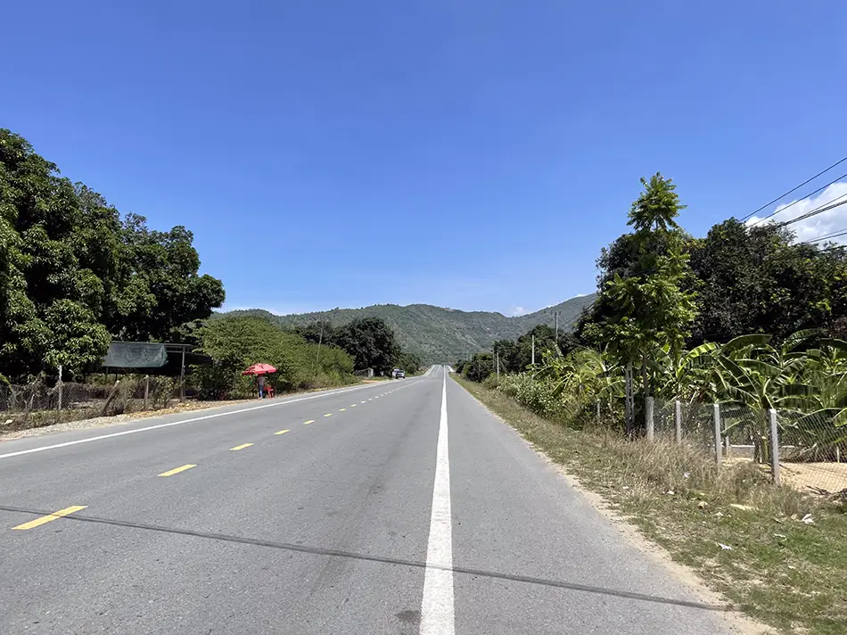 An empty bypass road in Vietnam with smooth pavement and a view of green rolling hills.