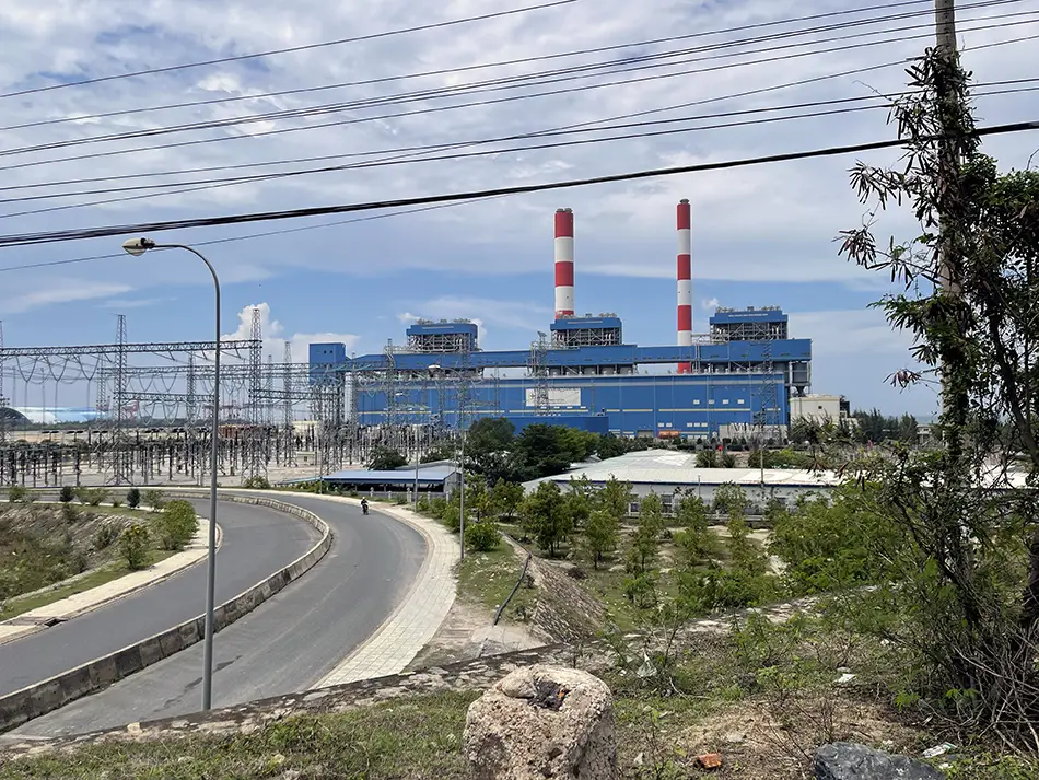 A road surrounded by lush green grass leading toward a striking, massive power plant building.
