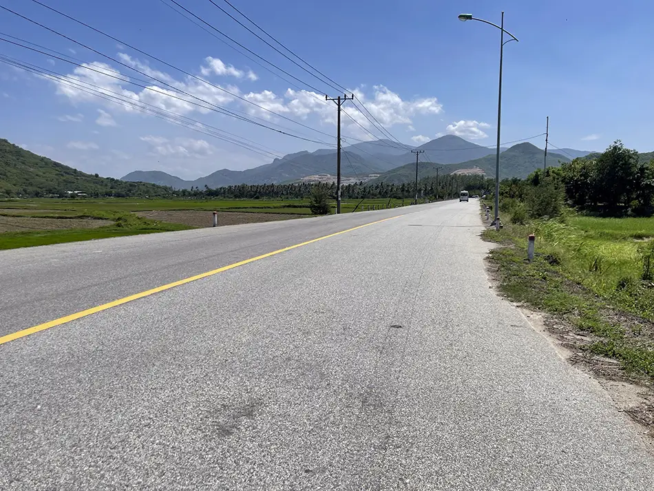 First-person view from the road showing smooth asphalt passing between lush green mountains.