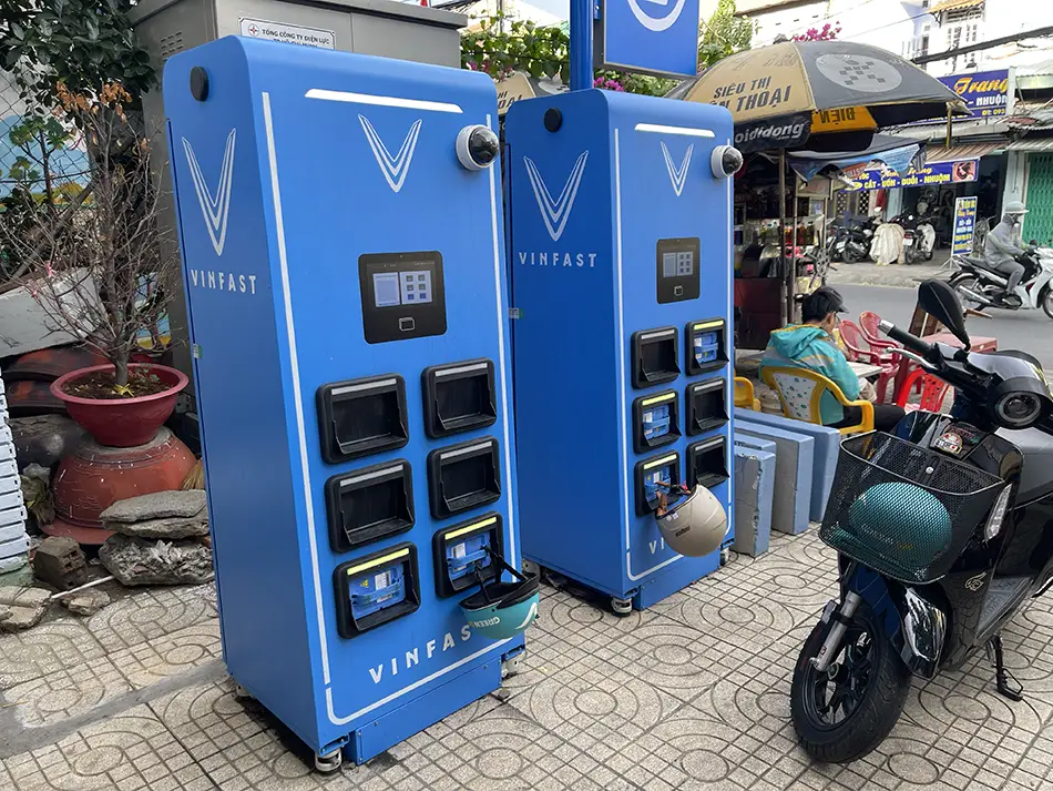 Blue battery swap station on a Saigon street with electric scooters parked nearby