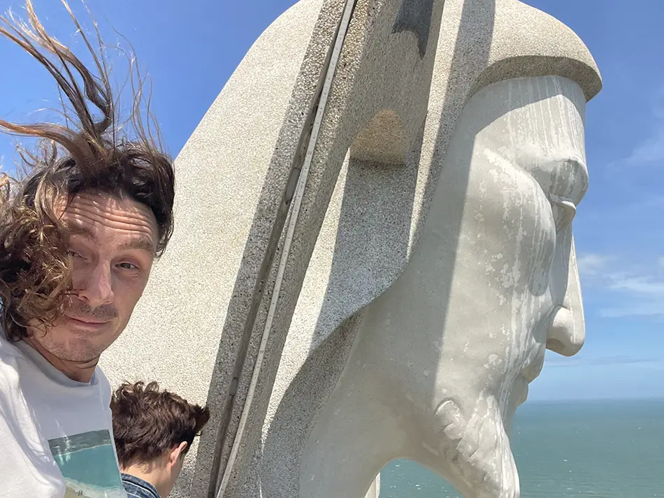 Selfie beside the head of the Christ the King statue, hair blown by wind.