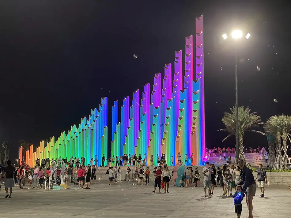 Tam Thang Tower at Back Beach in Vung Tau at night, its 143 concrete columns lit in rainbow LED colors while visitors walk through the plaza.