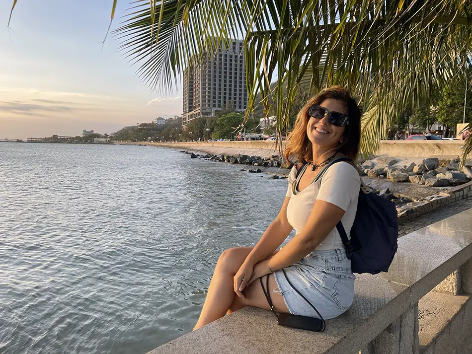 A female traveler with a backpack sitting on a seafront railing at Front Beach promenade