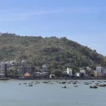 Panoramic view of Vung Tau city with a densely forested mountain rising behind the bay, waterfront buildings and roads stretching along the calm shoreline