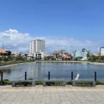 Vung Tau lake with a wide concrete promenade and trees lining the path, the kind of urban scene visitors encounter on a Vung Tau day trip from Ho Chi Minh City.