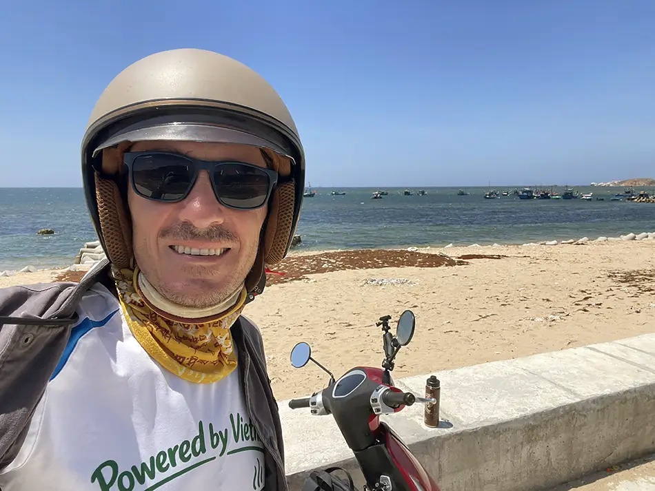Yuri Malykh standing with an electric scooter on a beach near the city of Phan Rang.