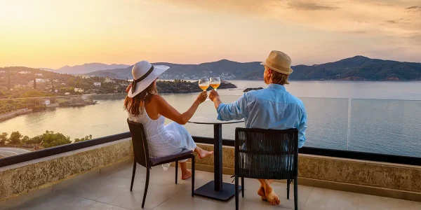 Couple enjoying wine tasting overlooking coastal landscape at sunset, representing wine travel experiences