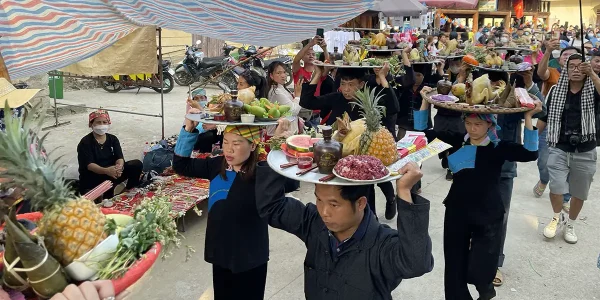 Villagers carrying trays of Vietnamese cuisine dishes as ceremonial festival offerings.
